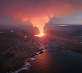 A red plume of lava near a town on a coastline