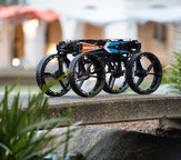A small, four-wheeled robot perches on a cement bridge with plants on either side.